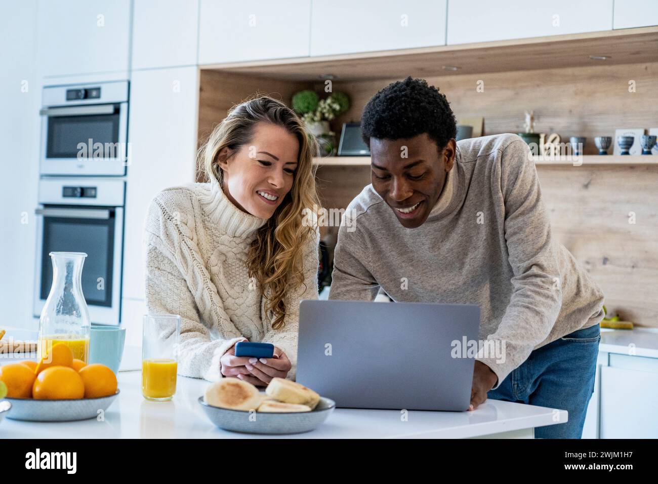 Cheerful adult couple using laptop together at kitchen counter Stock Photo