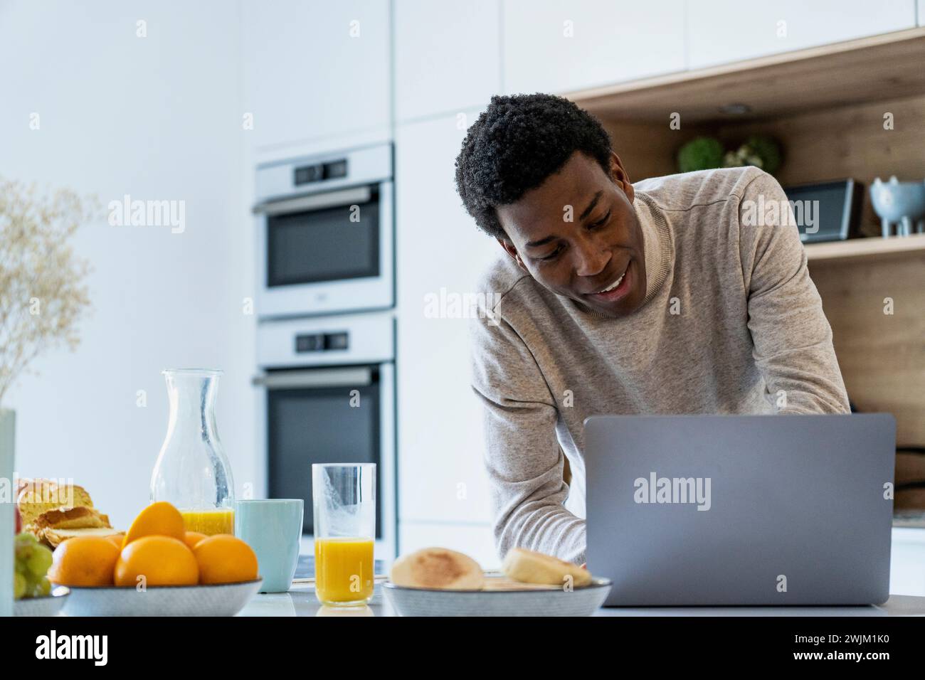Adult man using laptop while leaning on kitchen counter Stock Photo