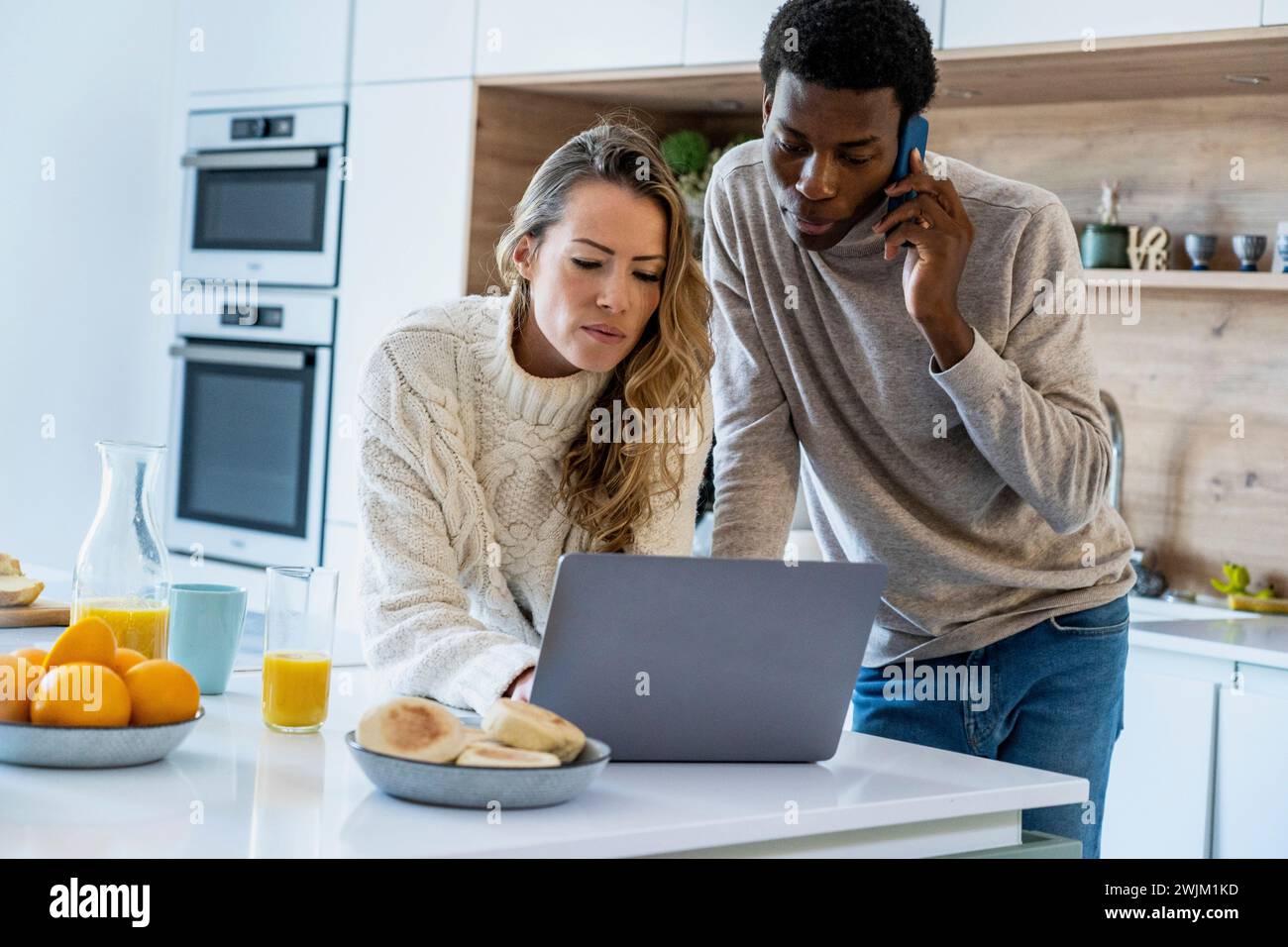 Adult couple using laptop while standing in kitchen Stock Photo