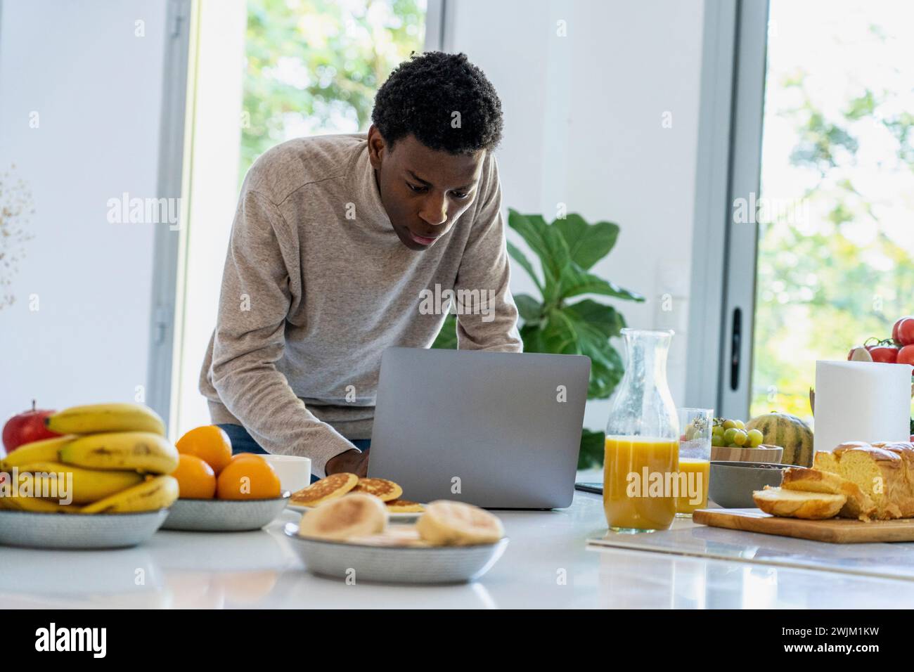 Adult man using laptop while standing at kitchen counter Stock Photo