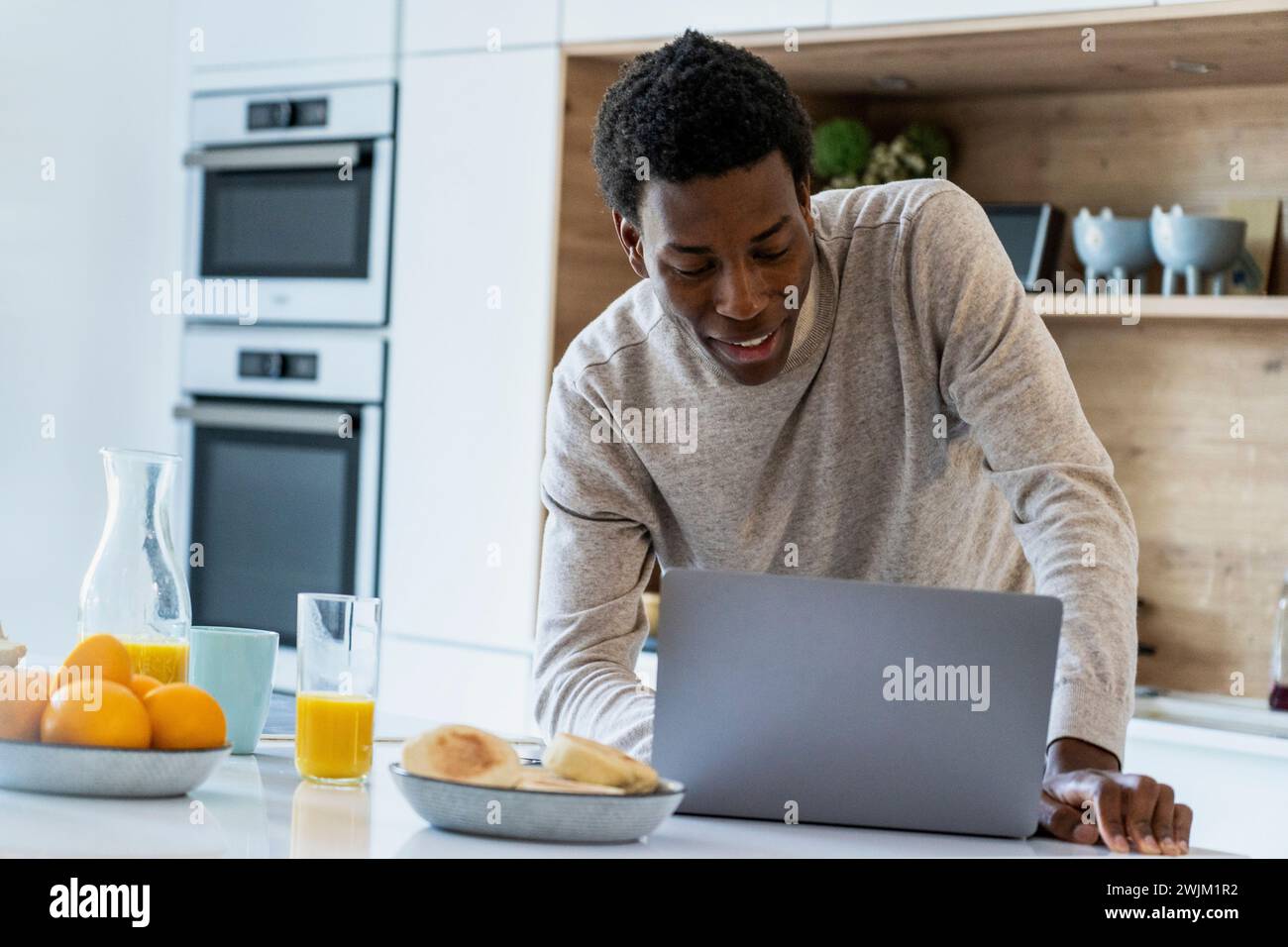 Adult man using laptop while leaning on kitchen counter Stock Photo