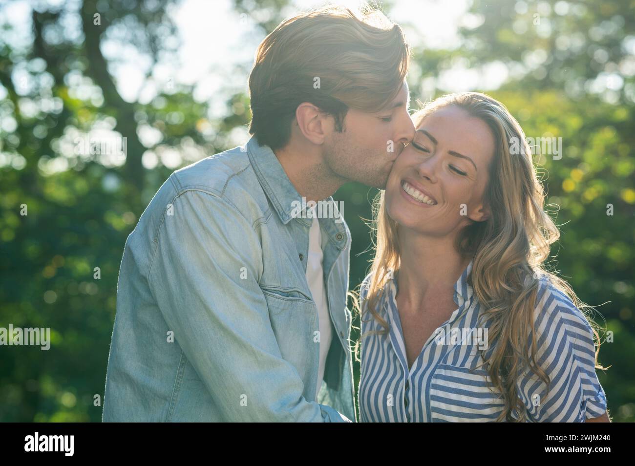 Adult man kissing girlfriend on the cheek while standing outdoors Stock Photo
