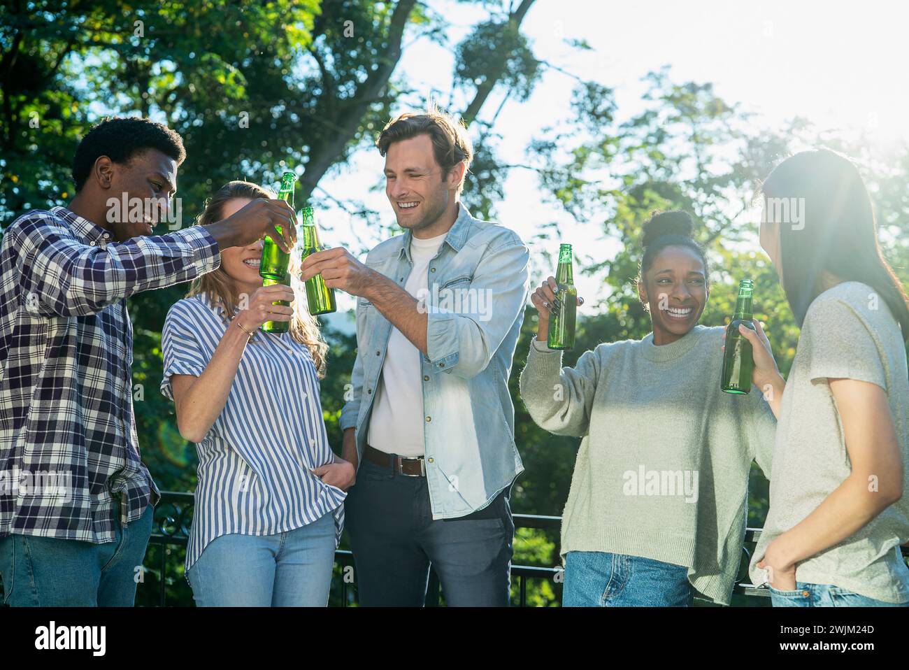Adult man celebrating with friends at rooftop toasting with beer bottles Stock Photo