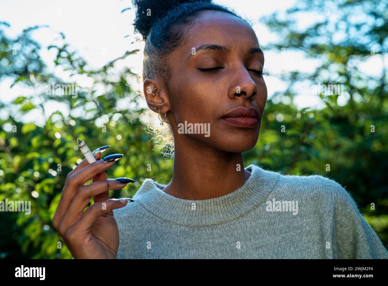 Adult woman smoking while standing outdoors with closed eyes Stock Photo