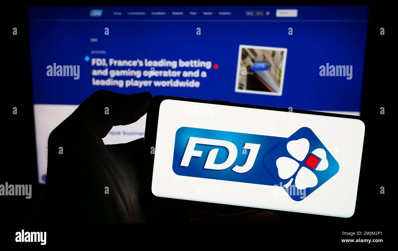 Person holding smartphone with logo of French lottery company Francaise des Jeux (FDJ) in front of website. Focus on phone display. Stock Photo