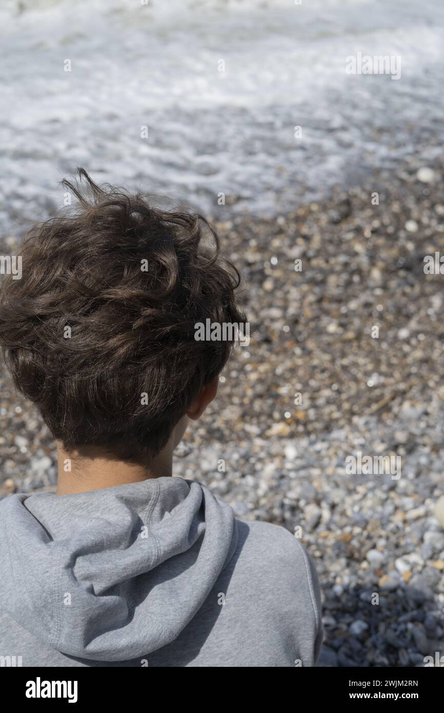Rear view of young person's head looking at seaside waves in Normandie Stock Photo