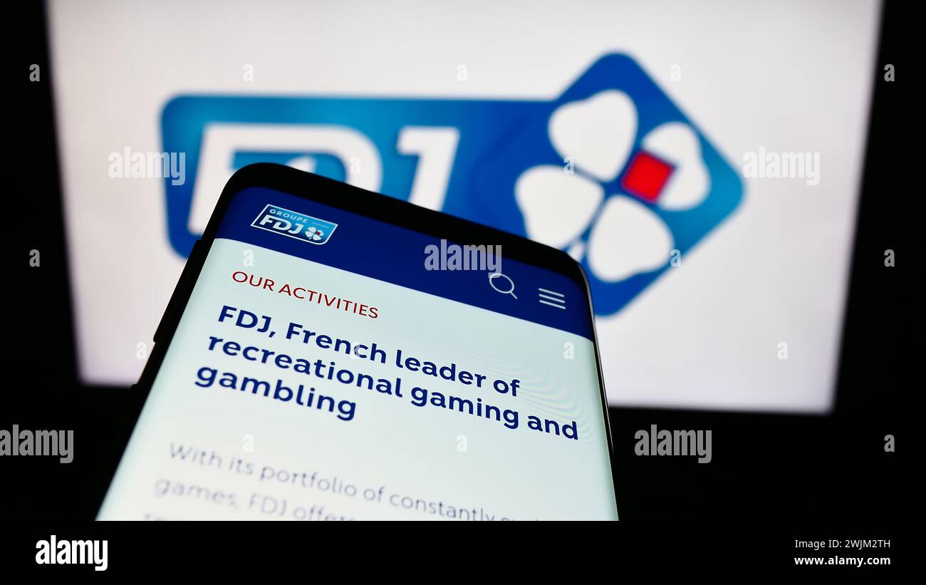 Smartphone with website of French lottery company Francaise des Jeux (FDJ) in front of business logo. Focus on top-left of phone display. Stock Photo
