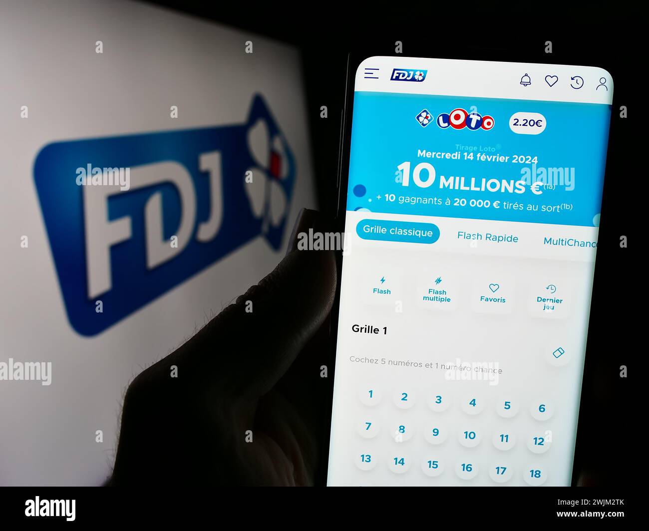 Person holding cellphone with webpage of French lottery company Francaise des Jeux (FDJ) in front of logo. Focus on center of phone display. Stock Photo