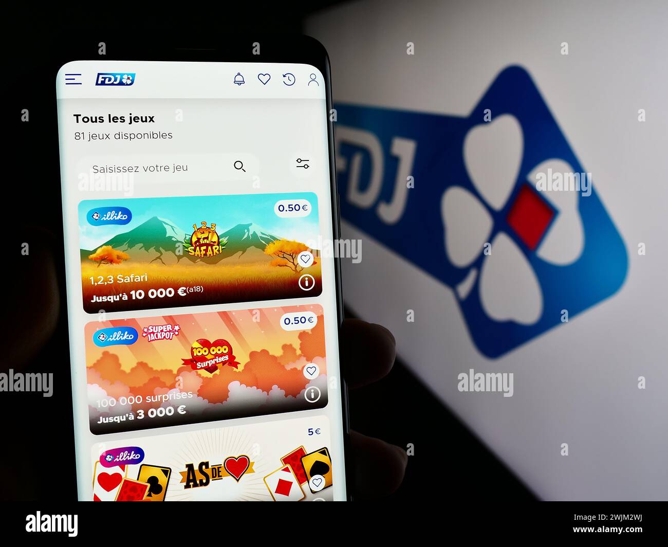 Person holding mobile phone with web page of French lottery company Francaise des Jeux (FDJ) in front of logo. Focus on center of phone display. Stock Photo