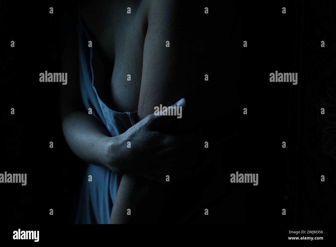 Dark image of woman's arm holding her torso Stock Photo