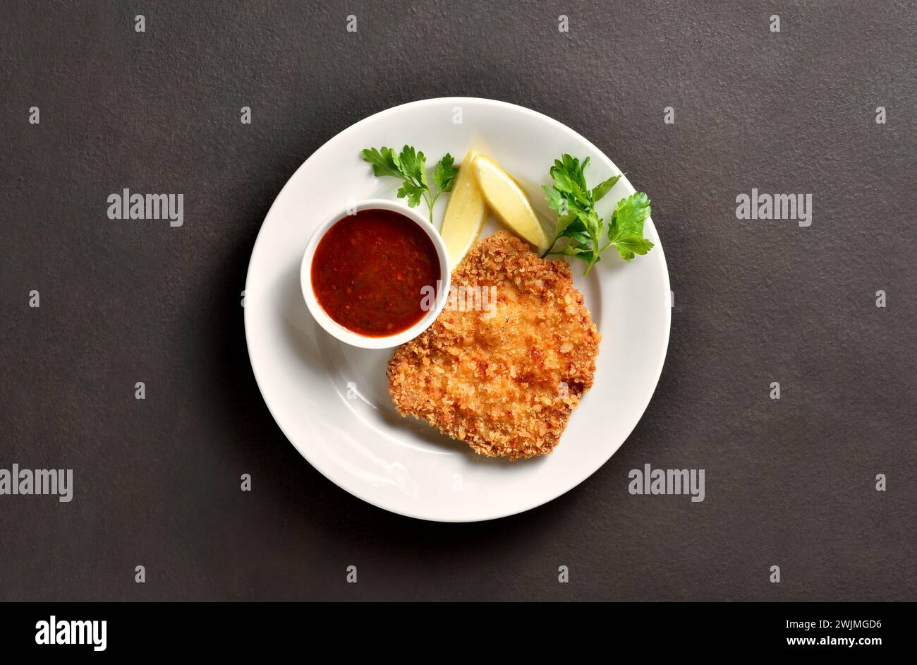 Schnitzel with lemon and leaves of parsley on white plate over brown stone background with copy space. Top view, flat lay Stock Photo