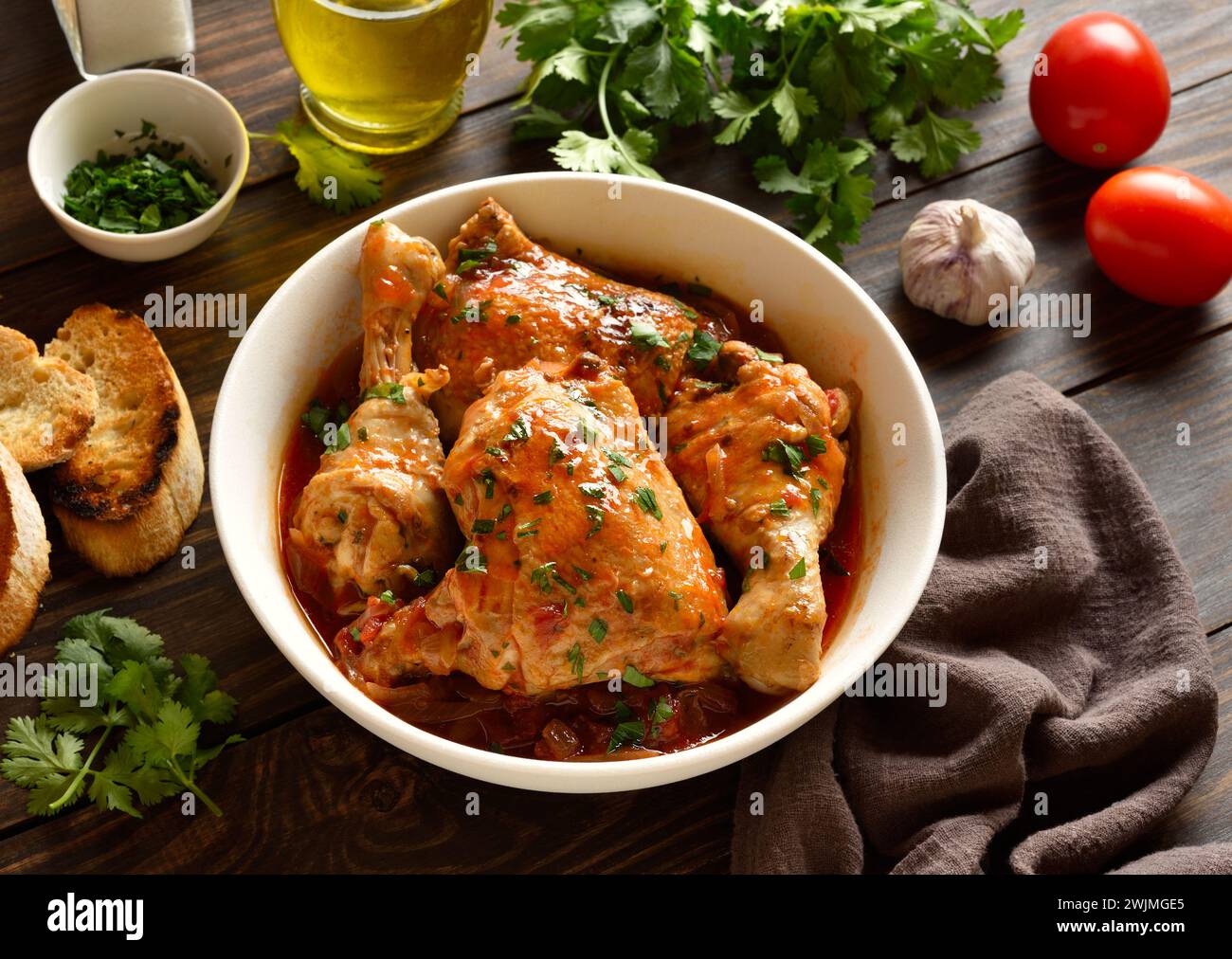 Georgian chicken stew with tomatoes and herbs (chakhokhbili) in bowl over wooden background. Baked chicken meat with tomato vegetable gravy. Healthy e Stock Photo