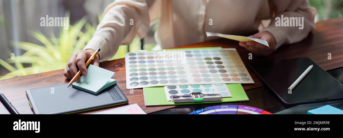 Creative graphic designer choosing color on color swatch and writing notes idea in adhesive note. Stock Photo