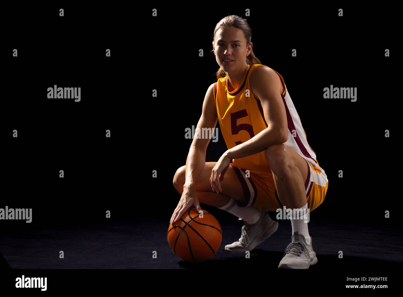 Athletic young woman in basketball gear poses with focus on black background. Stock Photo