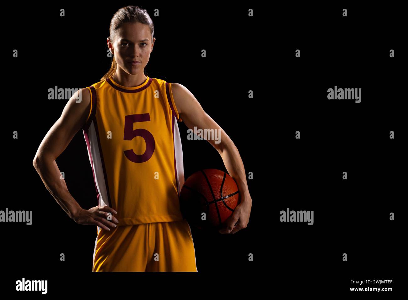 Athletic woman in basketball gear shows determination on black background. Stock Photo