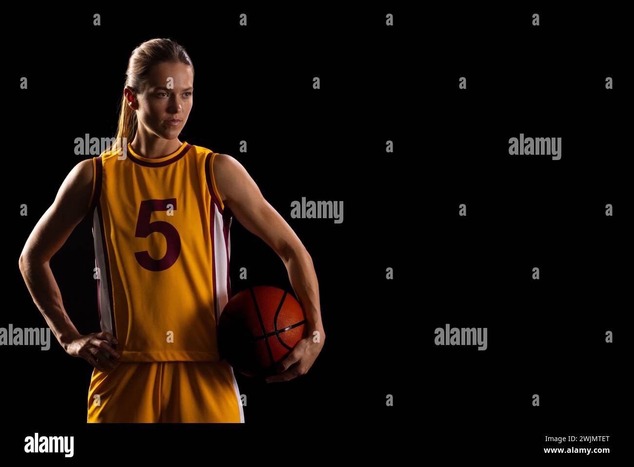 Female basketball player shows determination in uniform on black background. Stock Photo
