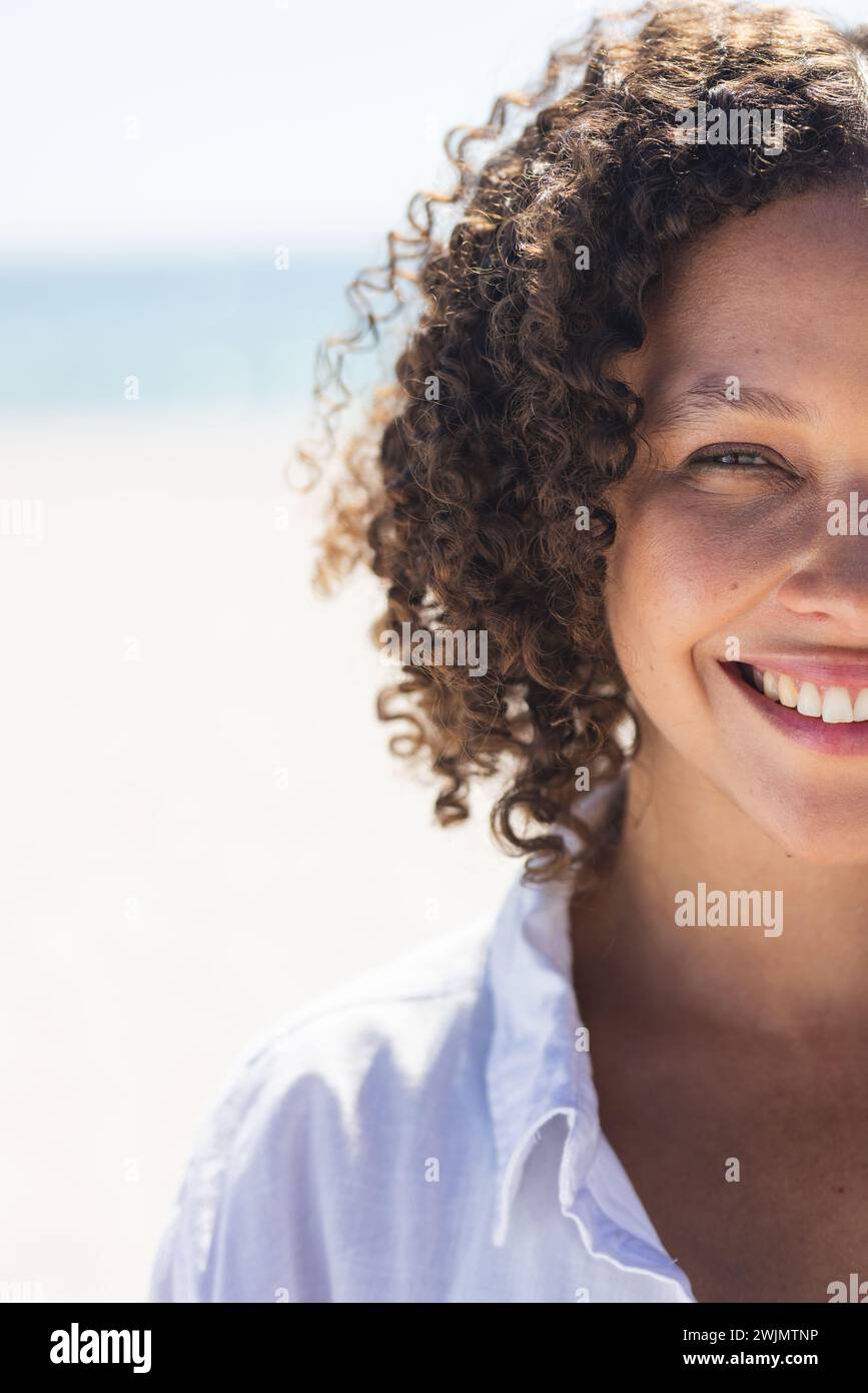 Young biracial woman smiles brightly at the beach Stock Photo