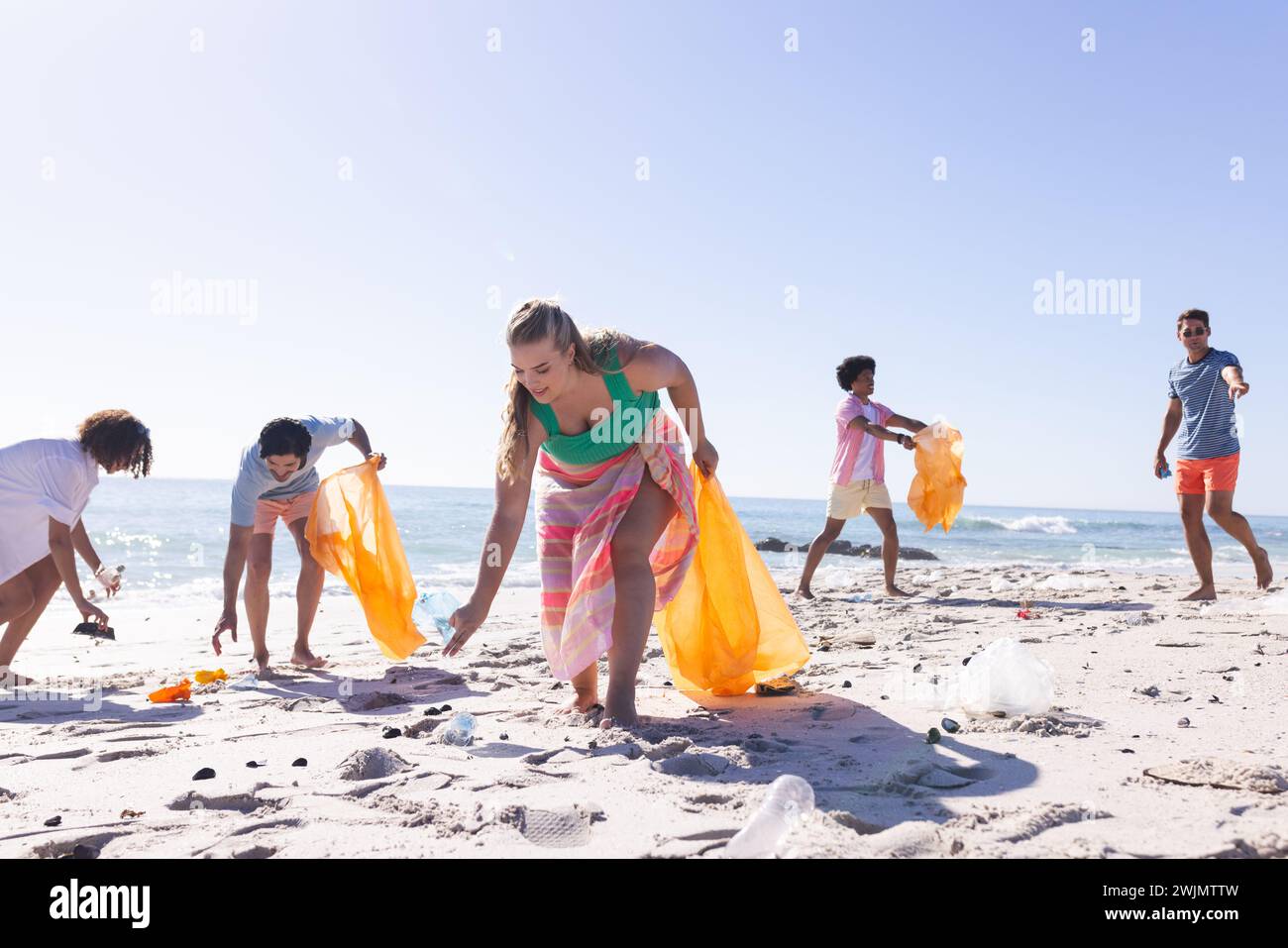 A diverse group of friends are cleaning up the beach and collecting trash with copy space Stock Photo