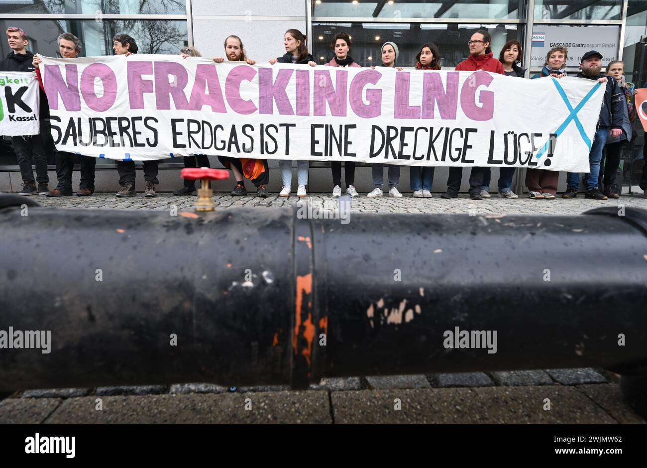 Kassel, Germany. 16th Feb, 2024. Behind the section of a pipeline, climate activists demonstrate against the Rügen LNG terminal with a banner reading 'No fracking LNG - clean natural gas is a dirty lie!' in front of the headquarters of gas network operator Gascade. The activists criticized the terminal on the Baltic Sea island and the further expansion of LNG import infrastructure in Germany as a climate crime. Credit: Uwe Zucchi/dpa/Alamy Live News Stock Photo