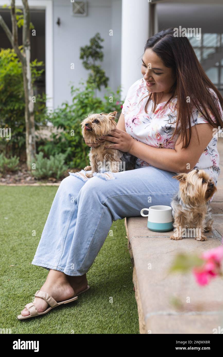 Young biracial plus size woman enjoys time with her dogs outdoors, with copy space unaltered Stock Photo