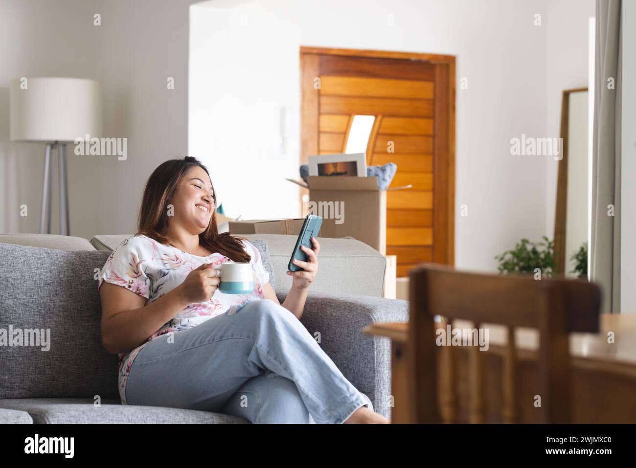 Plus-size biracial woman happily video calls amid moving boxes at home. Stock Photo