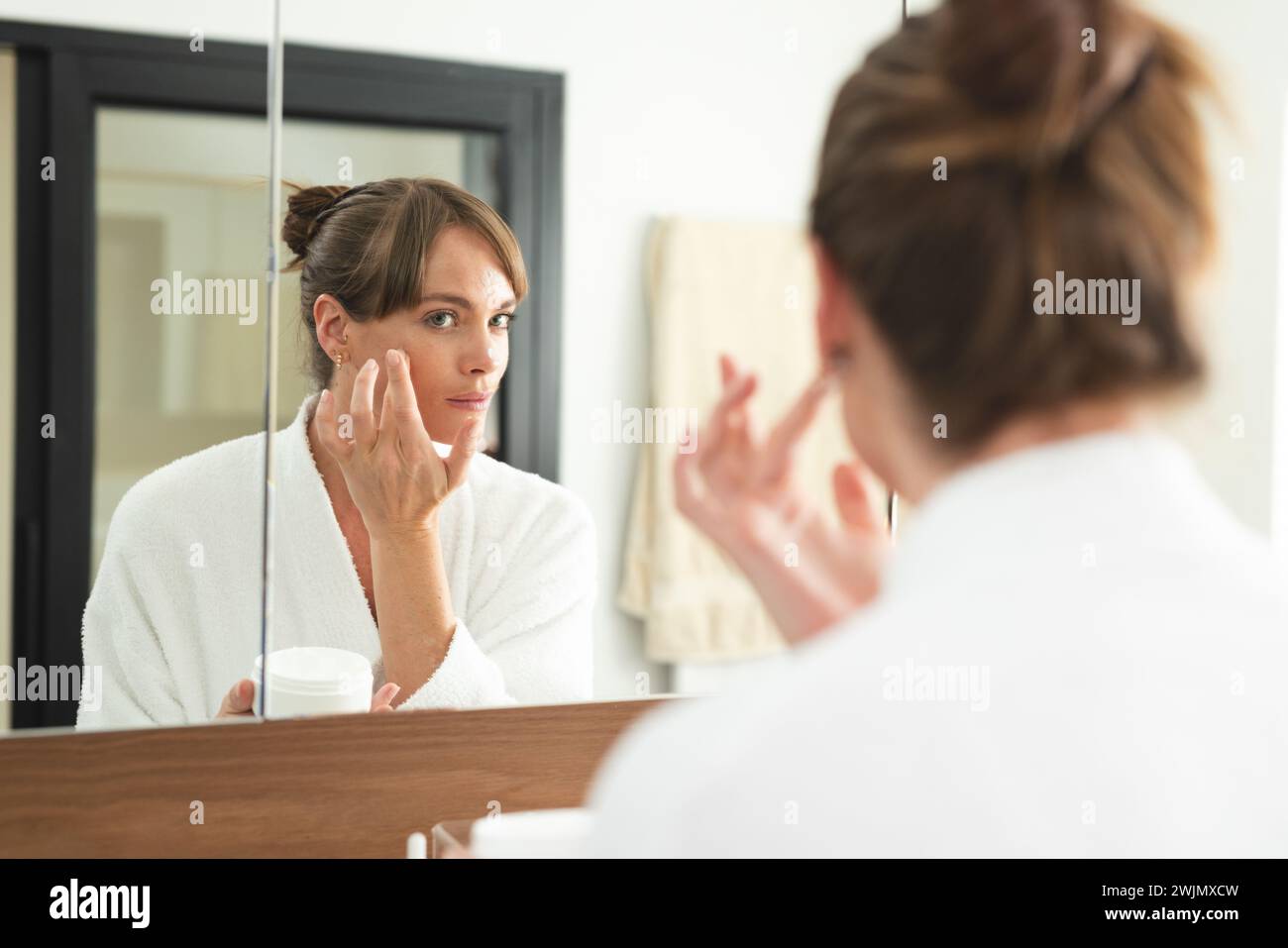 Caucasian woman applies cream to her face at home Stock Photo