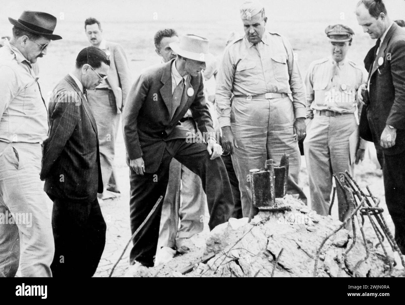 J. Robert Oppenheimer (in light colored hat), General Leslie Groves (large man in military dress to Oppenheimer's left), and others at the ground zero site of the Trinity test after the bombing of Hiroshima and Nagasaki, New Mexico 1945. Stock Photo