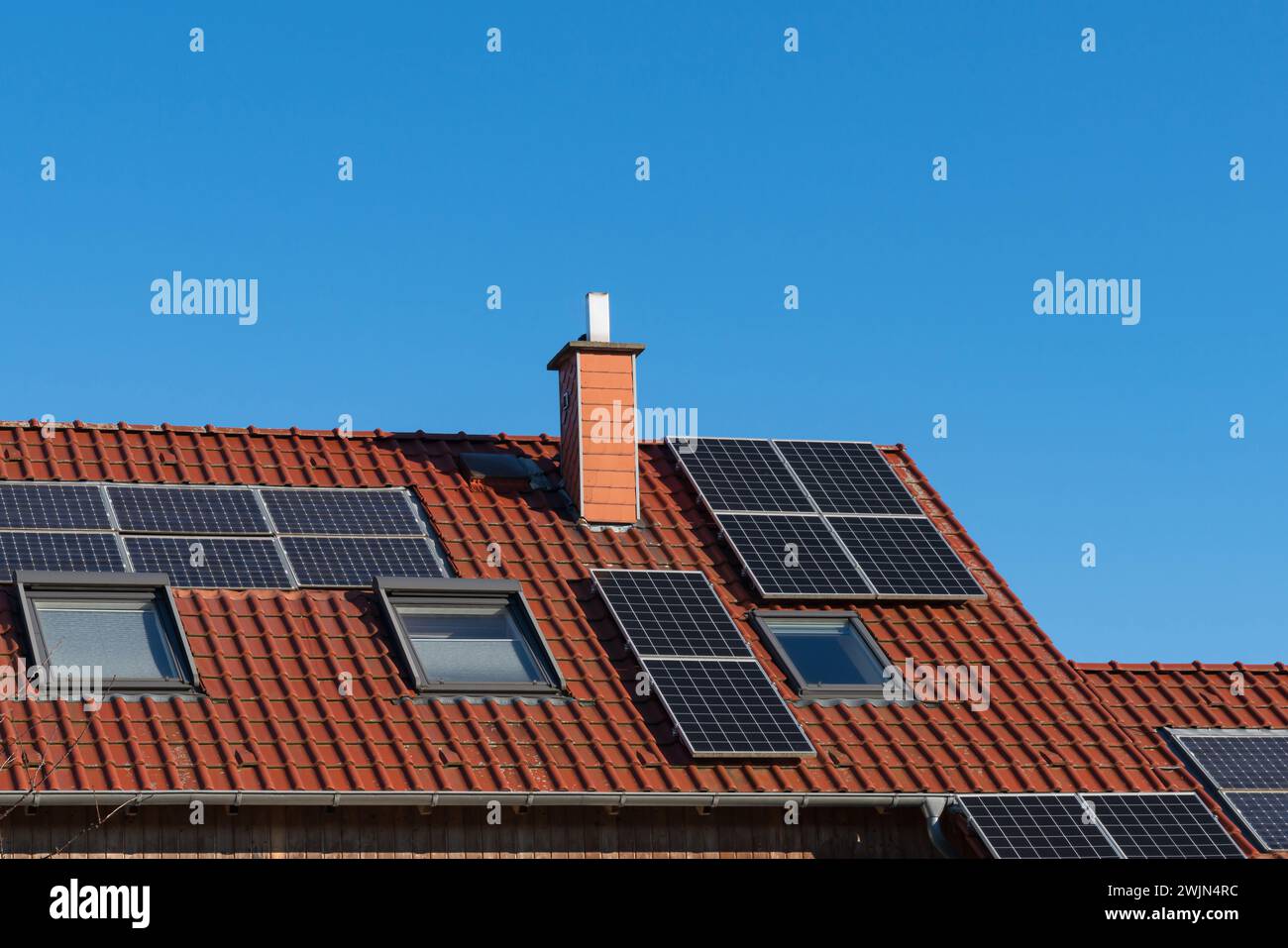 Tiled roof of a house with a chimney and solar panels under a blue sky ...