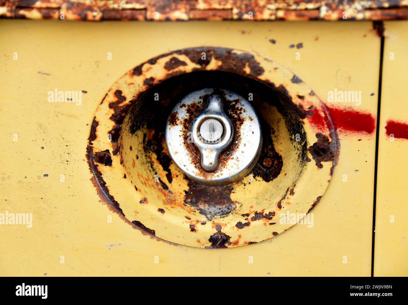 Rust surrounds a silver gas cap on a yellow vehicle. Image shows a