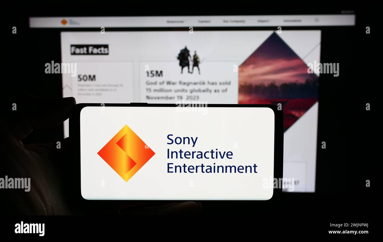 Person holding cellphone with logo of American video game company Sony Interactive Entertainment LLC in front of webpage. Focus on phone display. Stock Photo