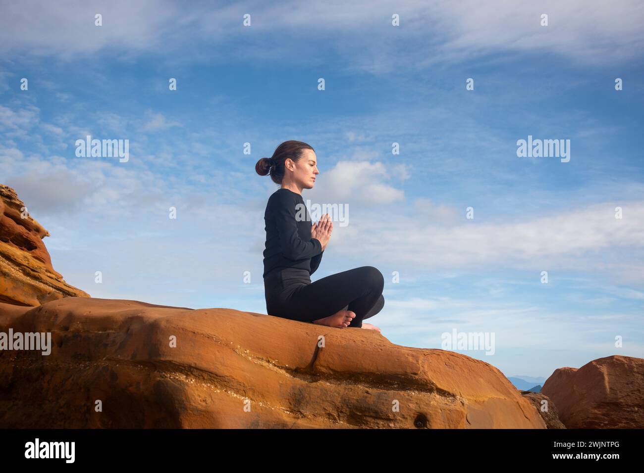 Woman meditating and practicing yoga on top of red rocks Stock Photo