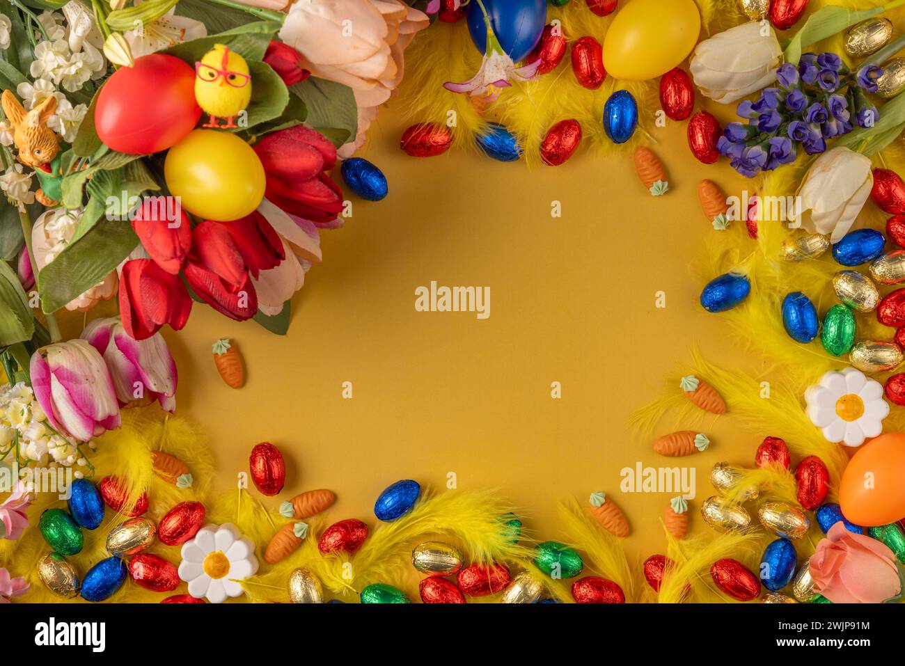 Colourful Easter frame with spring flowers, feathers, chocolate eggs and Easter eggs on a yellow background Stock Photo