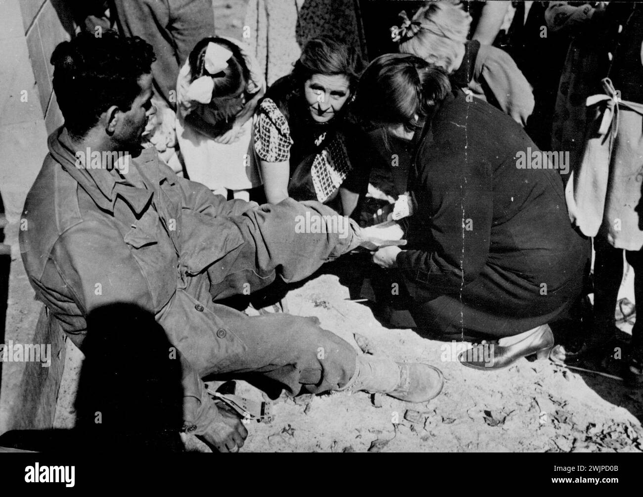 Belgians Aid Wounded U. S. Soldier -- Wounded in the swift allied advance through Belgium, an American infantryman has his foot bandaged by Belgian residents of the fortress town of Eben-Emael while his comrades push on toward the Netherlands and Germany. Rising against their oppressors, the Belgians gave valuable aid to the Allies, who had liberated most of the country less than three weeks after the first spearheads crossed into its borders on Sept. 2, 1944. November 10, 1944. Stock Photo