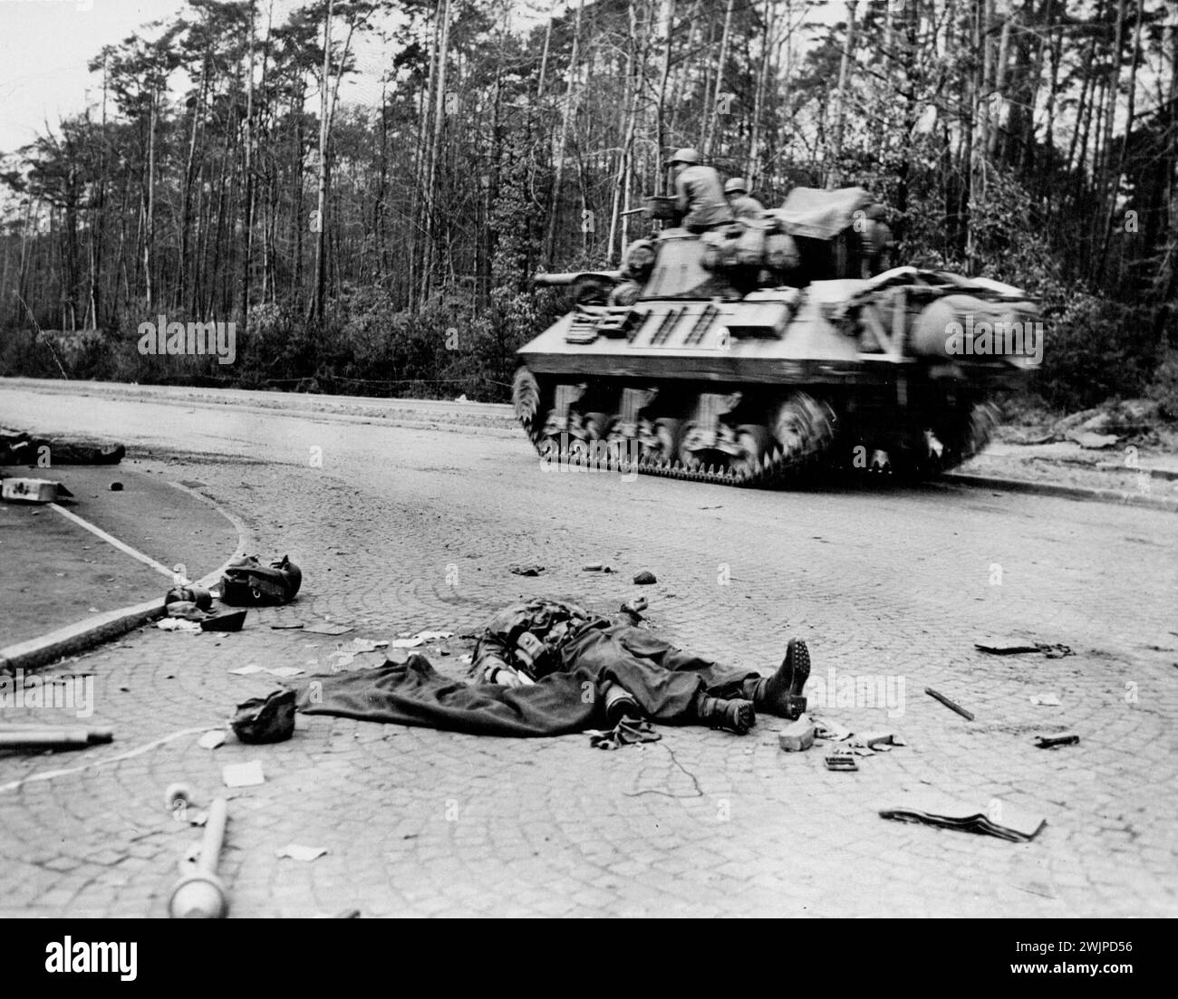 U.S. Tank Speeds Toward Frankfurt -- A tank of the sixth armored, third U.S. Army, speeds past two dead Nazi bazooka gunnors lying surrounded by seattered equipment it heads toward Frankfurt, Germany, march 27, 1945. Third army units cleared the city, 17 miles coast of the Rhine River, March 29. March 2, 1945. (Photo by U.S. Office of War Information Picture). Stock Photo