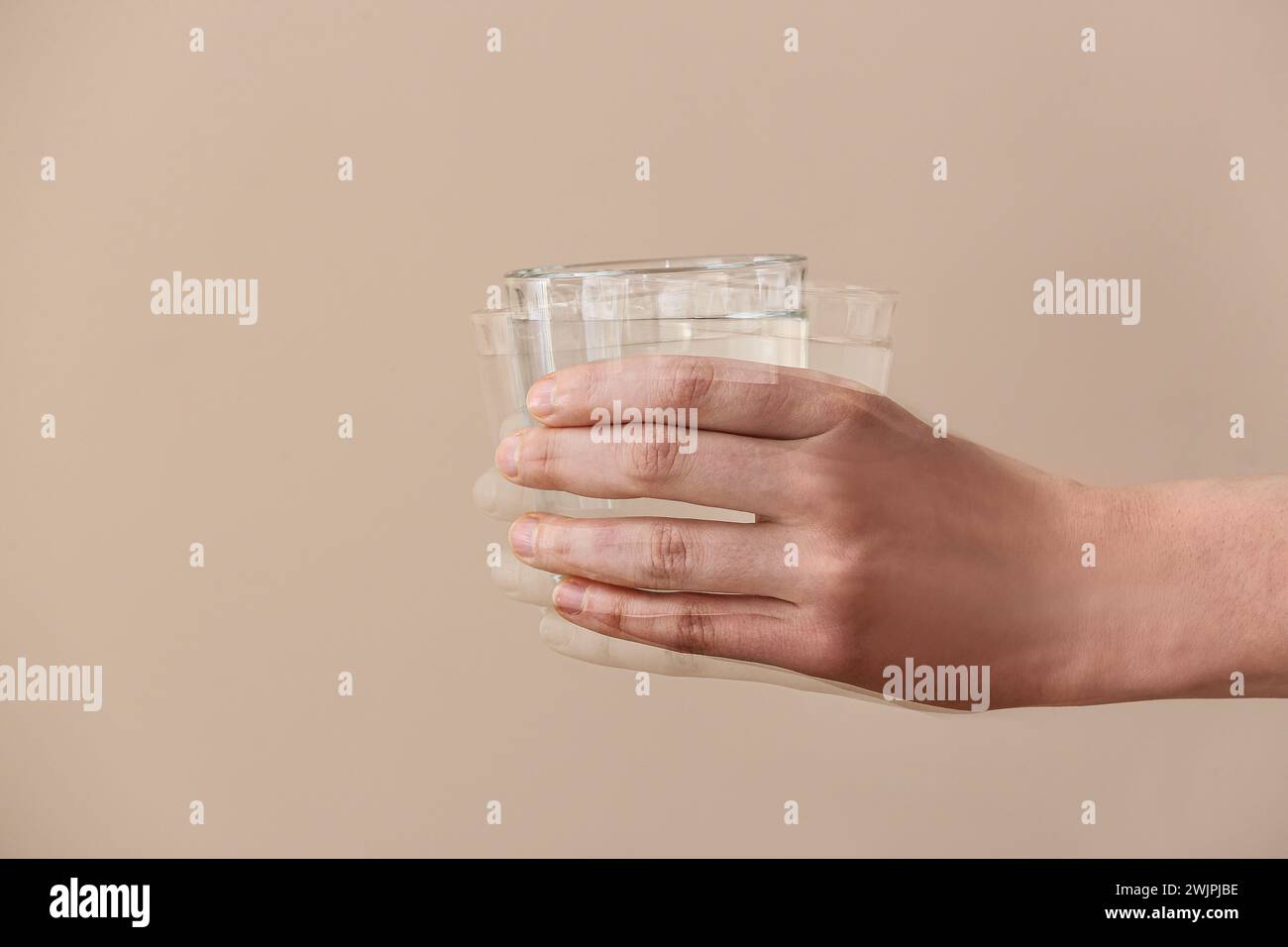 Trembling hand with glass of water on beige background. Parkinson's Awareness Month Stock Photo