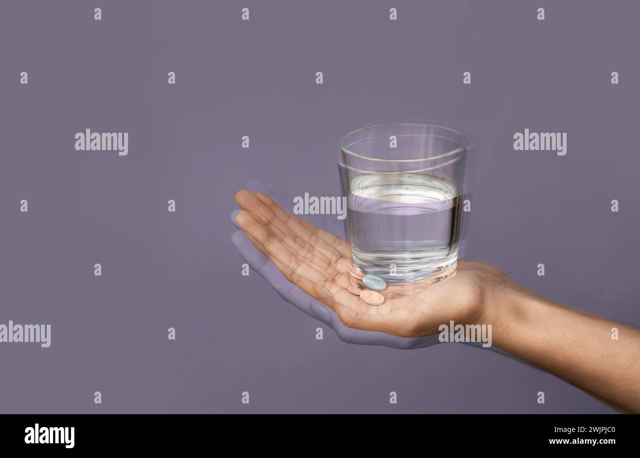 Trembling hand with glass of water on color background. Parkinson's Awareness Month Stock Photo