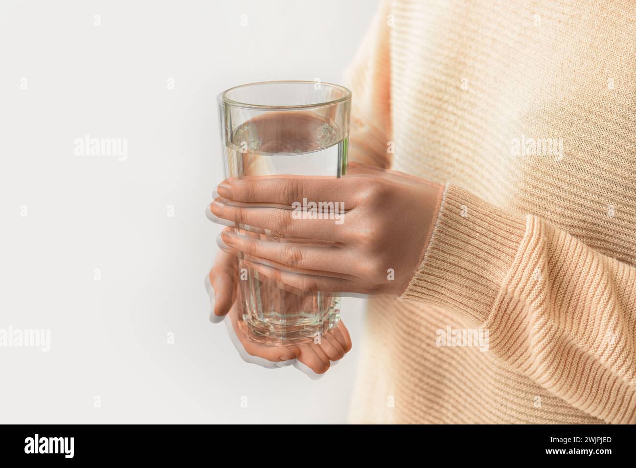 Woman holding glass of water in trembling hands on light background, closeup. Parkinson's Awareness Month Stock Photo