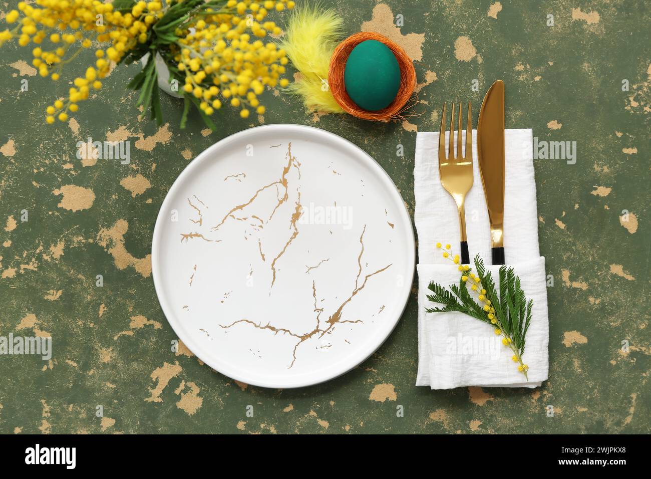 Stylish table setting for Easter celebration with Easter egg and mimosa on green background Stock Photo
