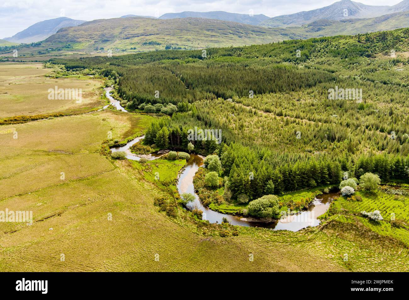 Aerial view of Joyce's river winding down below in Connemara region in Ireland. Scenic Irish countryside landscape with magnificent mountains on the h Stock Photo