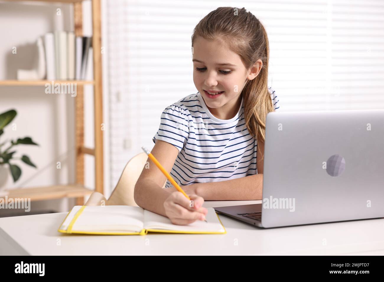 E-learning. Cute girl taking notes during online lesson at table ...