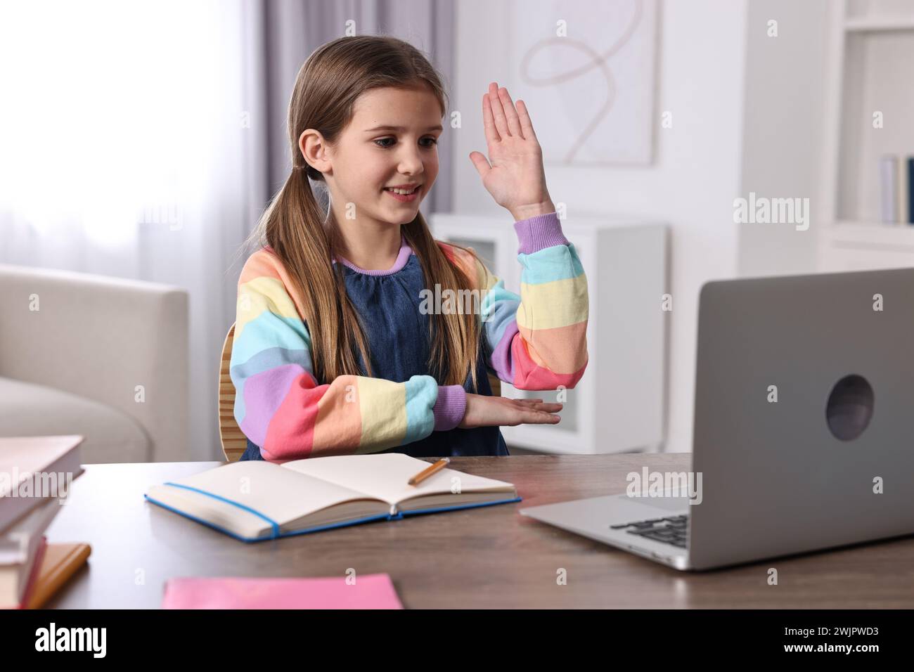 E-learning. Cute girl raising her hand to answer during online lesson ...