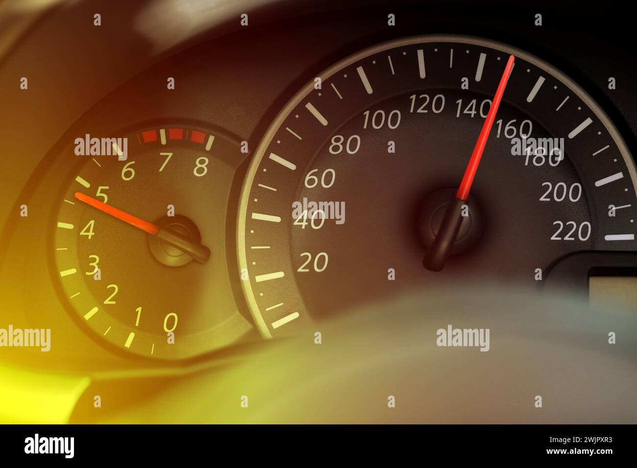 Speedometer and tachometer on car dashboard under yellow light, closeup ...