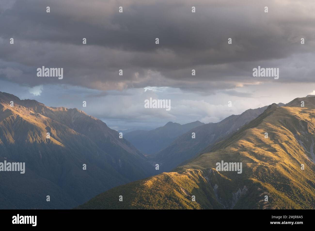 Scenic Mountain Sunset: Stunning Light Bathing Majestic Peaks Amidst Dramatic Clouds Stock Photo