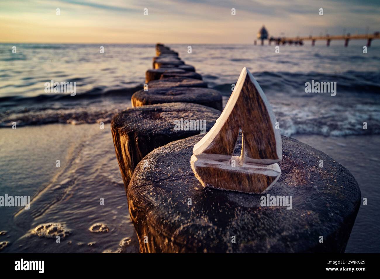 Wooden sailboat model on coastal breakwater at sunset, symbolizing travel and exploration. Stock Photo