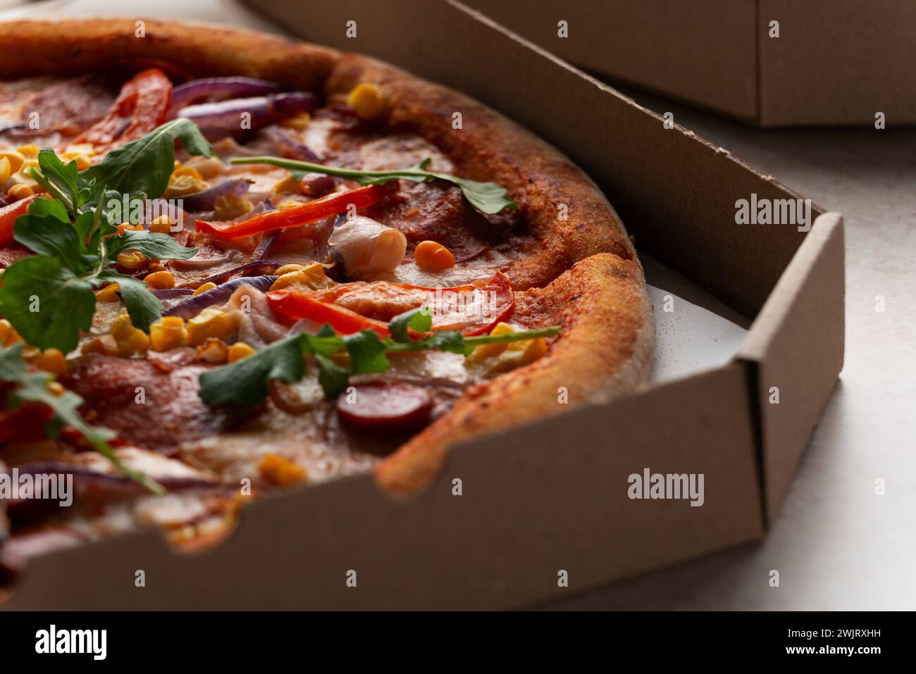 Large Pizza with sausages peppers and sweetcorn in open carton box on kitchen table extreme closeup view Stock Photo