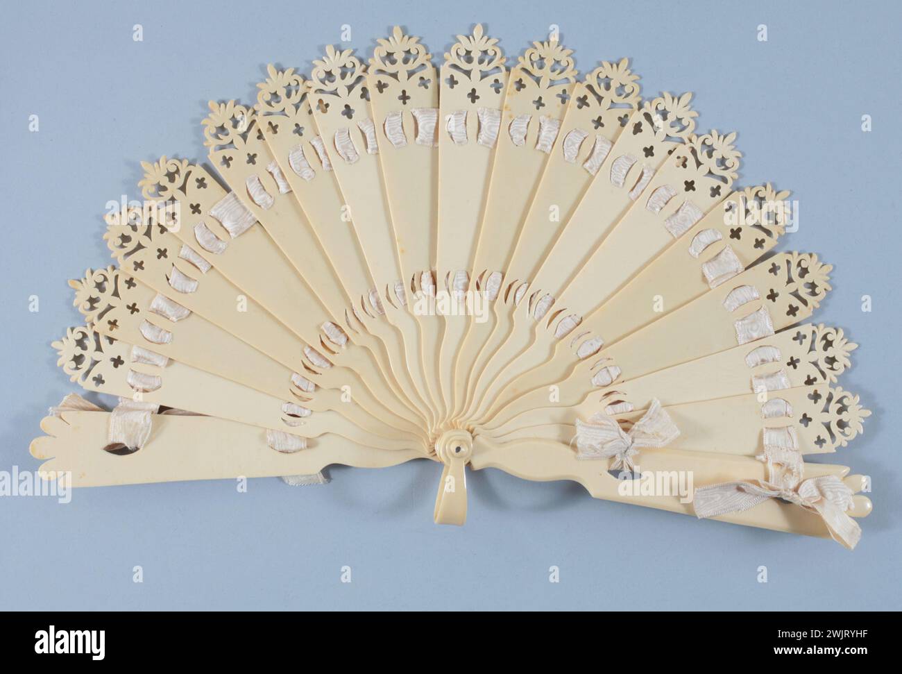 Broken fan, decor: high strands finer in pinnacle with ripple pattern, at the base 3 small crosses, 2 thicker plumes with trilobed patterns, 2 passages of moire ribbon ended by knots passing in eyelets fitted into the plumes . Gal1997.116.1 Celluloid, Moire Crème ribbon Stock Photo