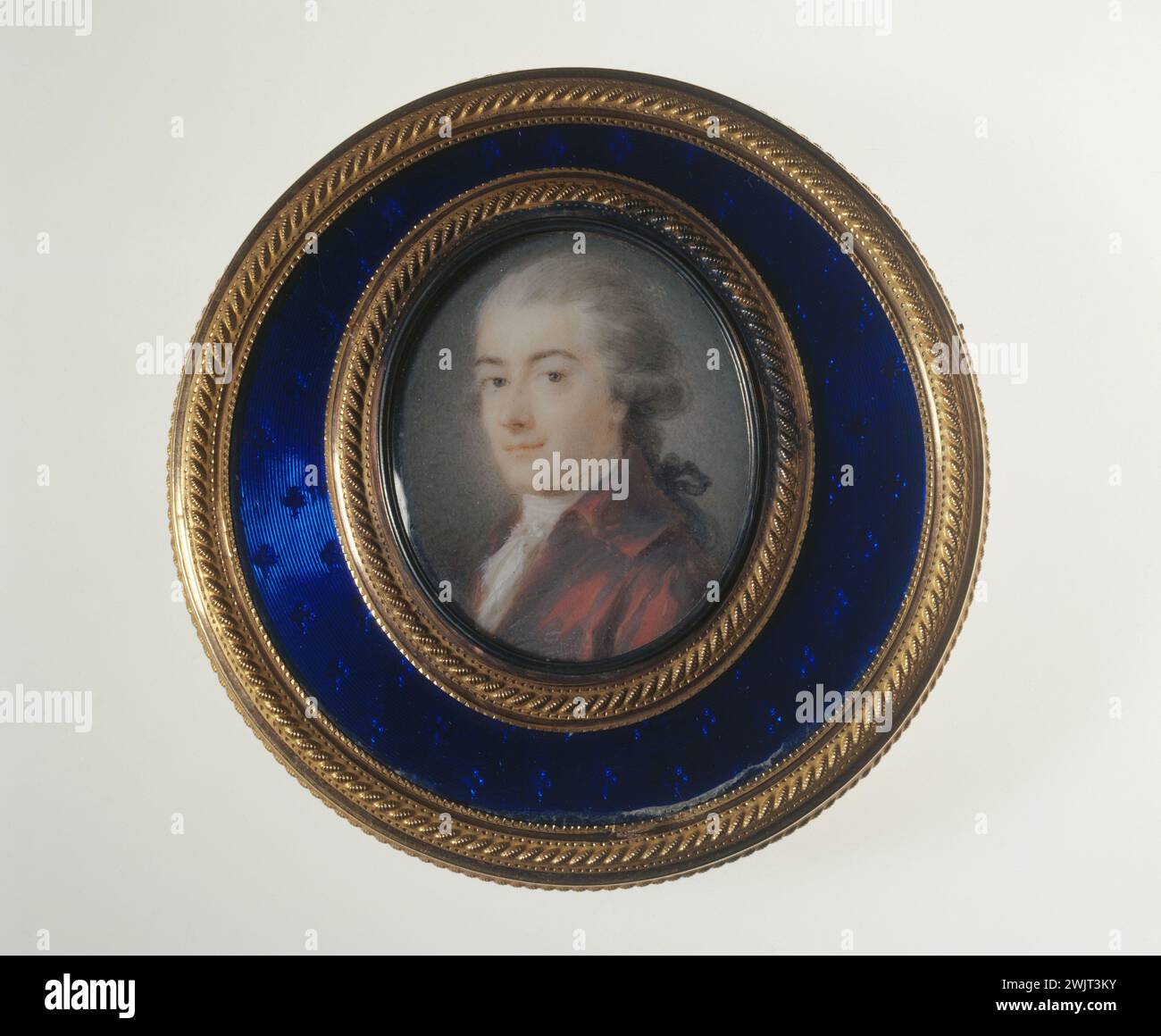 Heinrich Friedrich Fuger (attributed to). Oval miniature in gouache sur ivoire representing a portrait of a young man in red clothes on the lid of a gold circular box, enamelled with blue on a guilloche gold background with decor of parallel circles dotted with clover and pea patterns, XVIIIth . Paris, Cognacq-Jay museum. 39178-1 Round box, blue email, ivory gouache, guilloche, red habit, young man, oval miniature, gold, gold, pea, portrait, trefle Stock Photo