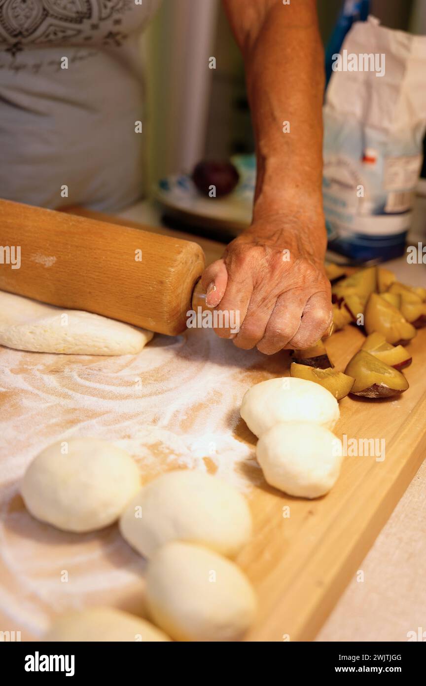Preparation of homemade fruit dumplings with plums. Czech specialty of sweet good food. Dough on kitchen wooden table with hands. Stock Photo