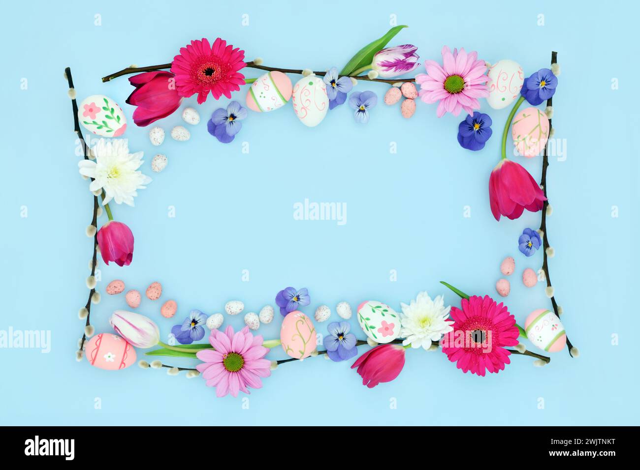 Happy Easter background border with edible and decorative eggs, flowers and willow branches on pastel blue. Flat lay. Natural nature frame design. Stock Photo