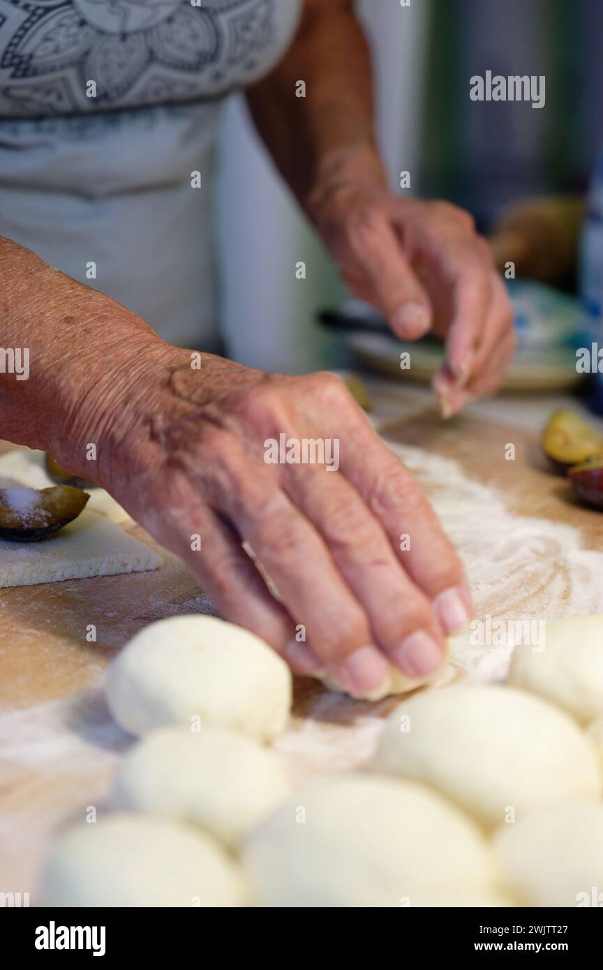 Preparation of homemade fruit dumplings with plums. Czech specialty of sweet good food. Dough on kitchen wooden table with hands. Stock Photo
